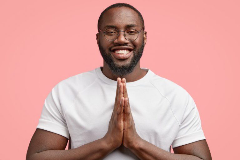 horizontal-shot-smiling-black-man-keeps-hands-pressed-together-believes-something-positive